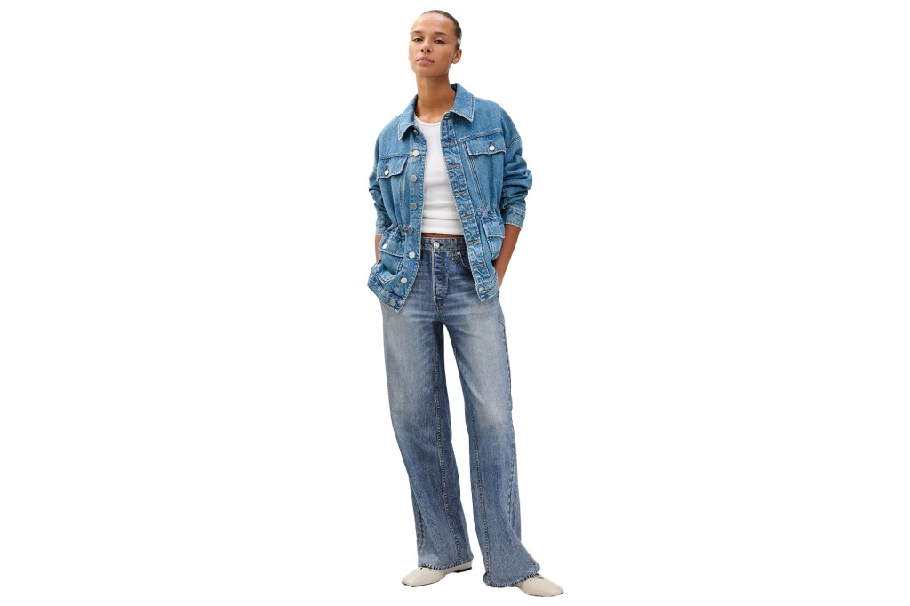 A woman wears a denim jacket with an elasticized waist over a white tank top and wide-leg jeans.