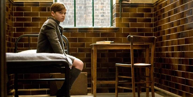 Young Voldemort sits on a bed in the orphanage in Harry Potter