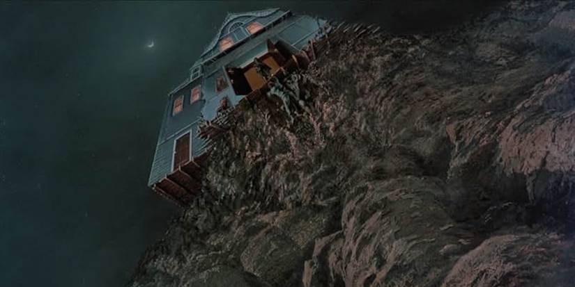Arthur Cobb (William Katt) stands precariously at the edge of the cliff where his house is suddenly placed.