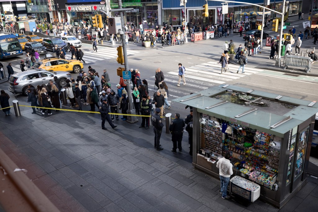 A large crowd of people, police, taxis, and cars near a newsstand and a cordoned-off area on a city street.