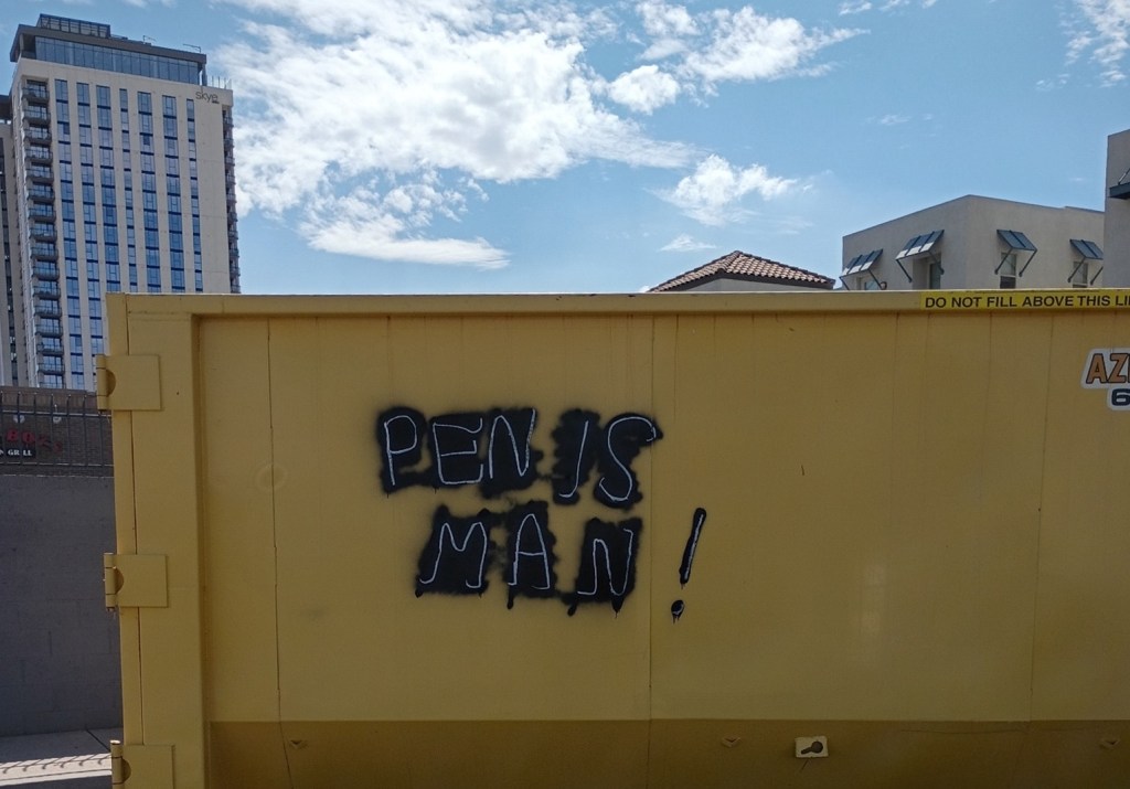 A yellow construction dumpster in downtown Tempe tagged with the words "PENIS MAN."