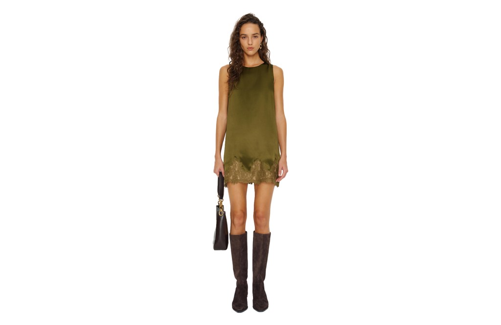 A model wearing a green mini slip dress with lace trim, brown boots, and carrying a matching brown handbag.