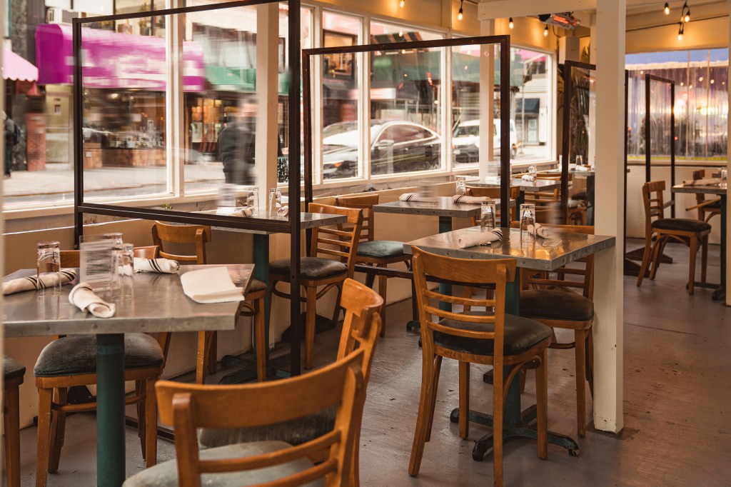 Outdoor dining area of a New York City restaurant set up on a sidewalk with empty tables and transparent partitions.
