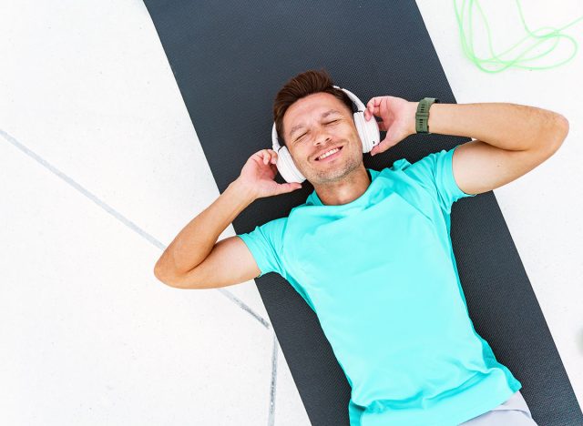 A man joyfully relaxes on a mat, eyes closed, immersed in music, embodying serene post-workout bliss.