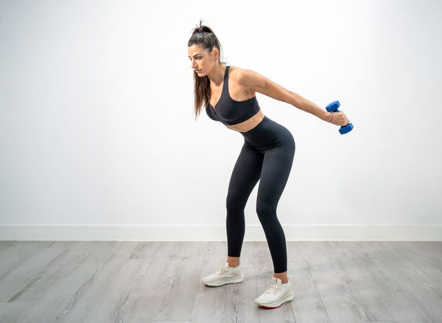 Woman doing tricep kickbacks using dumbbells with arms extended backward and leaning forward