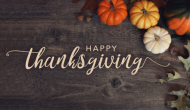 Happy Thanksgiving text with pumpkins and leaves over dark wood background