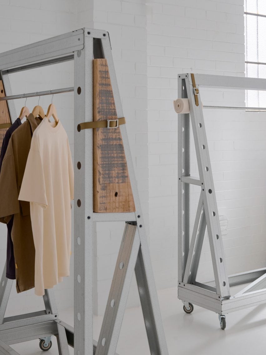 Minimalist clothing rack setup with industrial steel frames and wooden panels, displaying neutral-toned shirts on hangers in a white studio space.