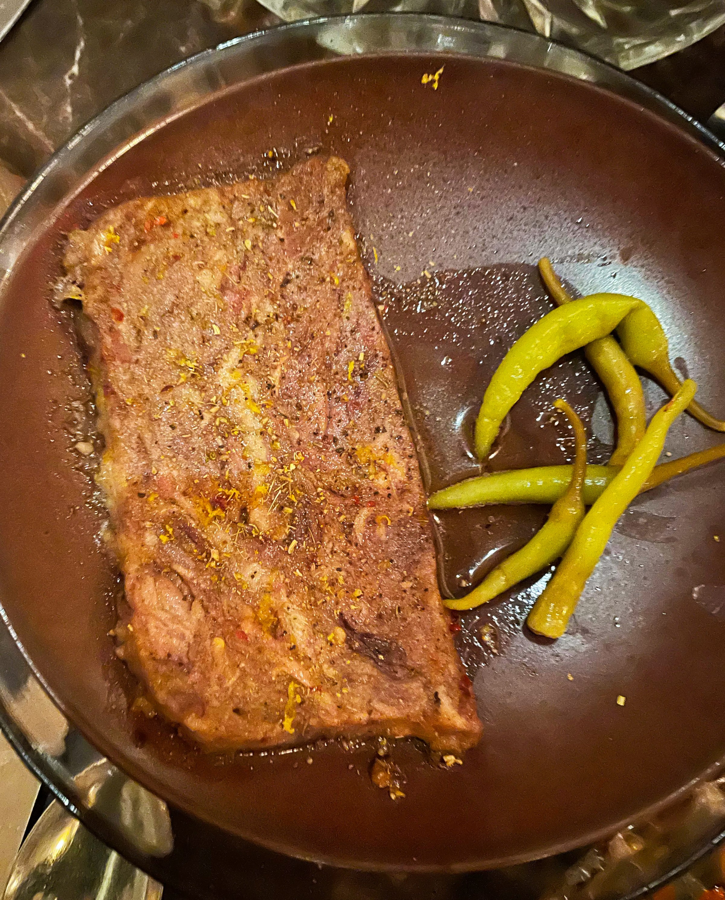 A crisped-meat on a brown plate next to peppers.