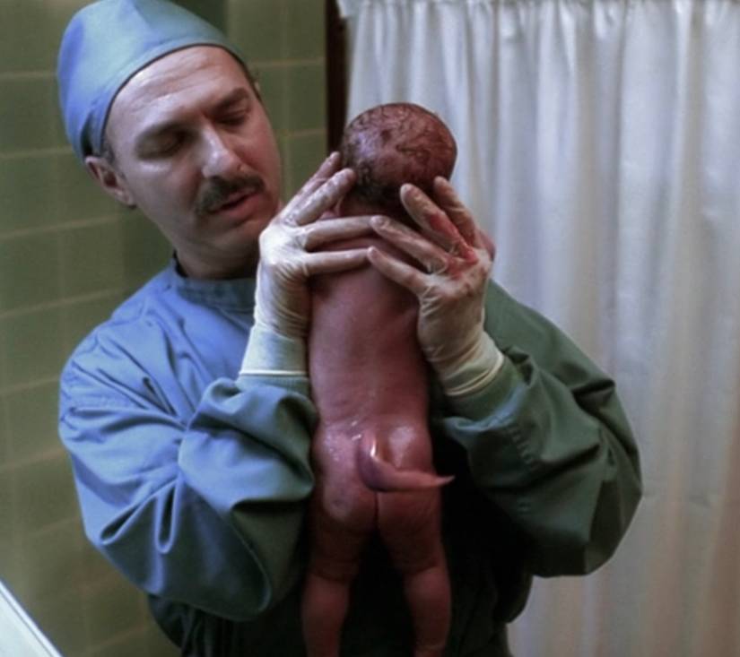 A doctor holds up a newborn baby with a tail in The X-Files episode "Small Potatoes"