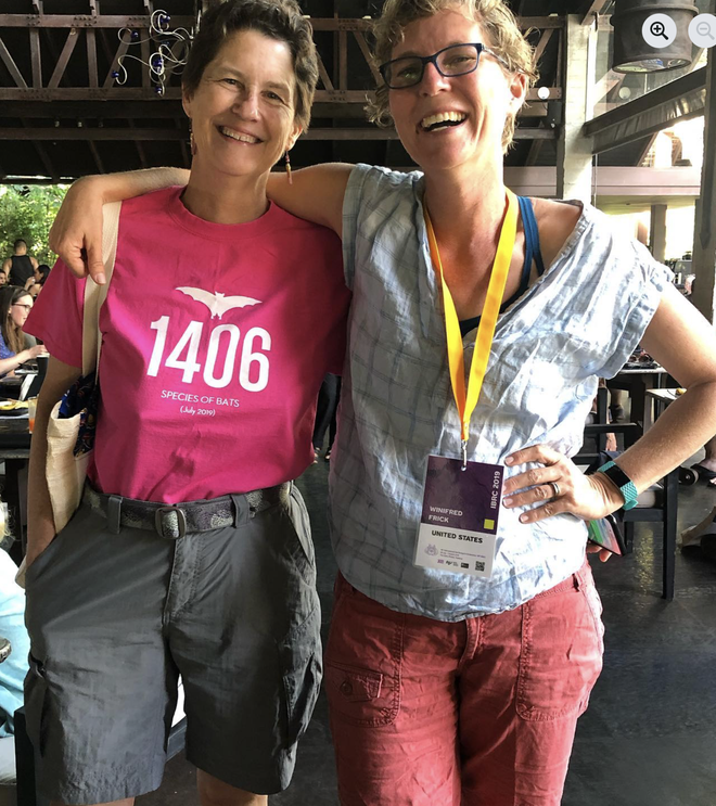 nancy simmons poses next to winifred frick wearing a pink t-shirt that reveals there were 1,406 bat species known by the time of the july 2019 international bat conference.