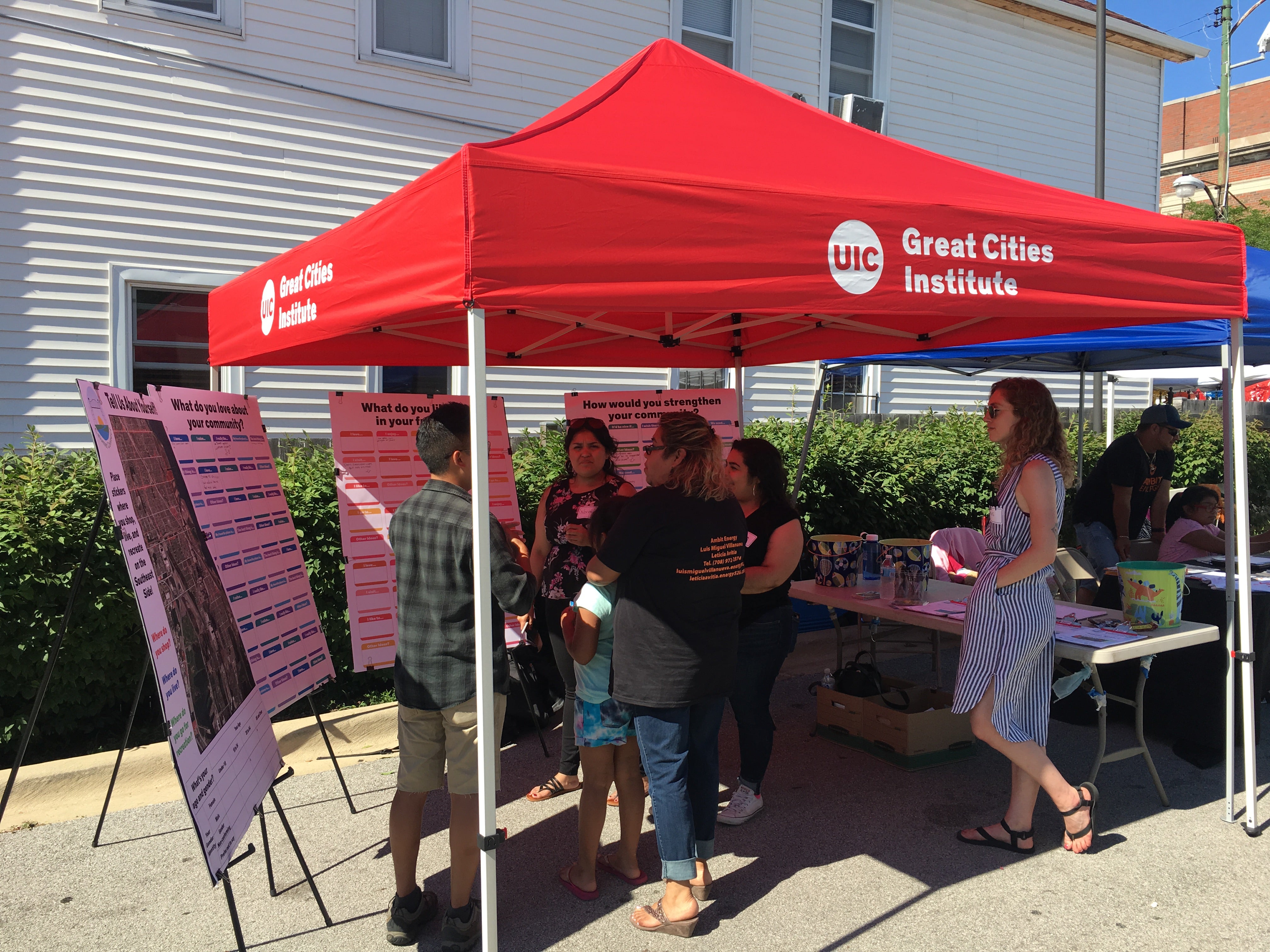 people talk under a red pop-up tent on a sunny day