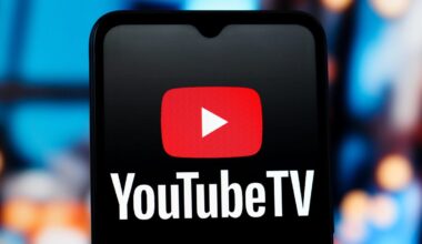 the YouTube TV logo on a black mobile phone in front of a blurry set of monitors