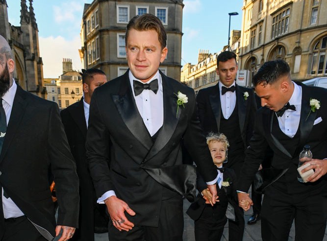 Adam Peaty and groomsmen walking with a young boy in a tuxedo.