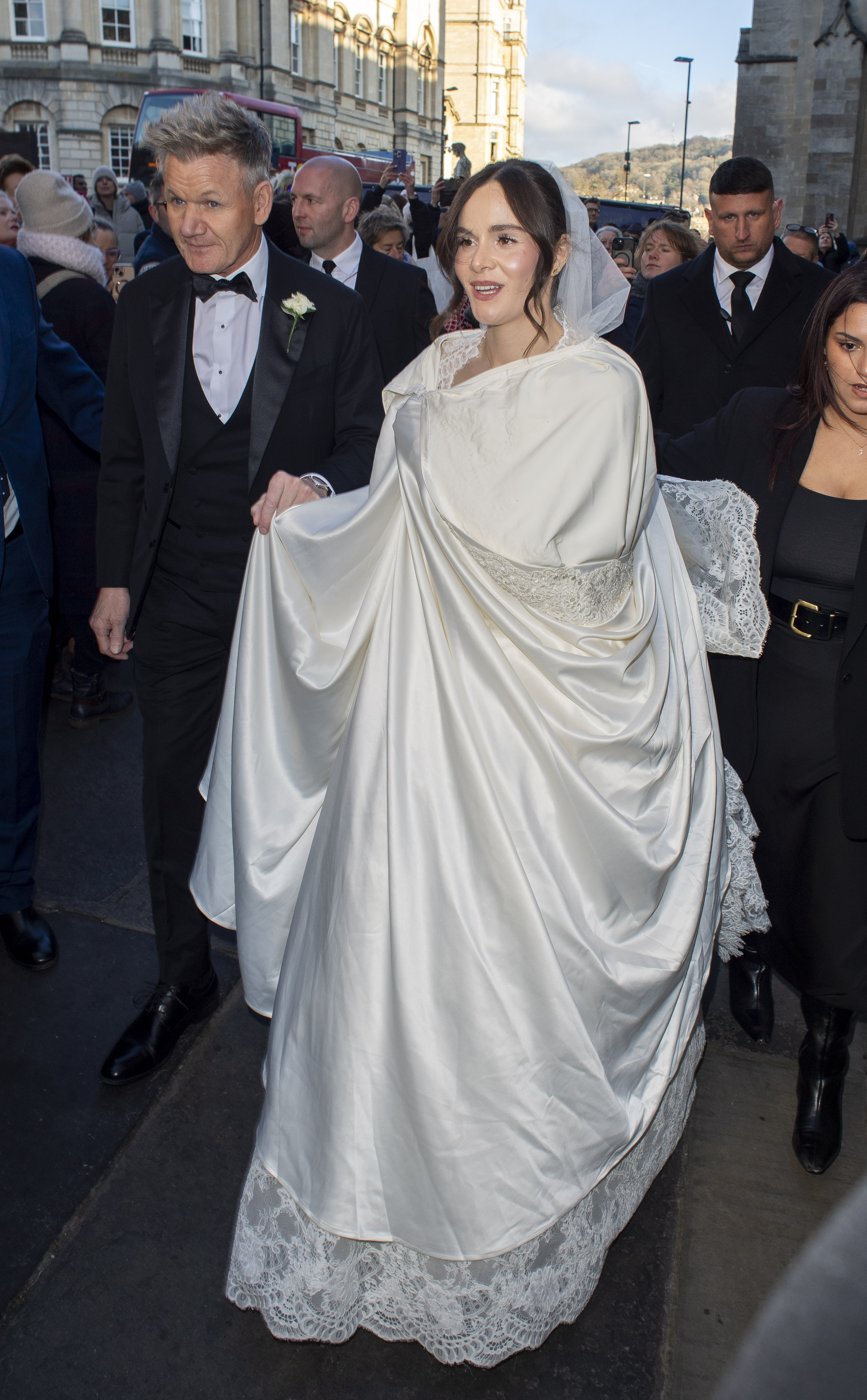 Holly Ramsay, wearing a white wedding dress and veil, arrives at Bath Abbey with Gordon Ramsay.