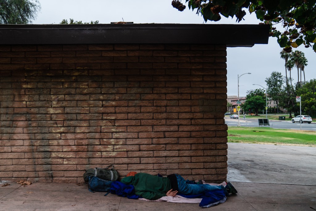 A homeless person sleeps on the ground at a park near Old Town on July 17, 2024. / Ariana Drehsler for Voice of San Diego