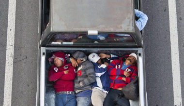 Aerial view of six people lying closely together in the bed of a pickup truck parked between two white lines on a road.