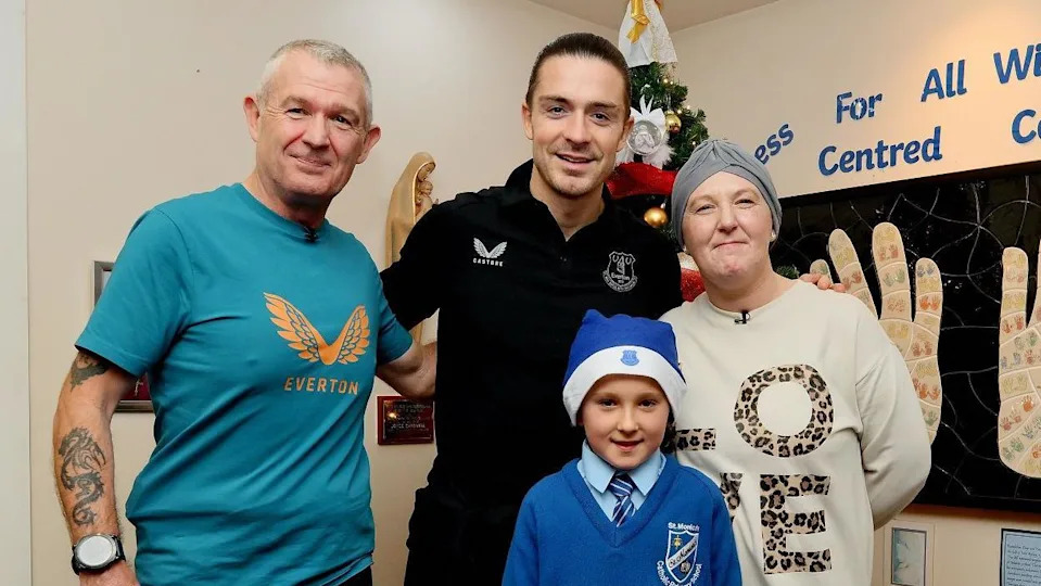 Group shot of Grealish with his arms around mum Gemma, wearing a grey turban cap and white jumper with the word Love, and grandad Keith in a blue Everton shirt on the left. Georgie in his blue Everton santa hat and blue school uniform stands in front of them.