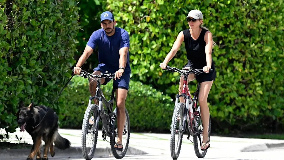 Joaquim Valente in a blue shirt rides a bike alongside Gisele Bündchen in a black shirt