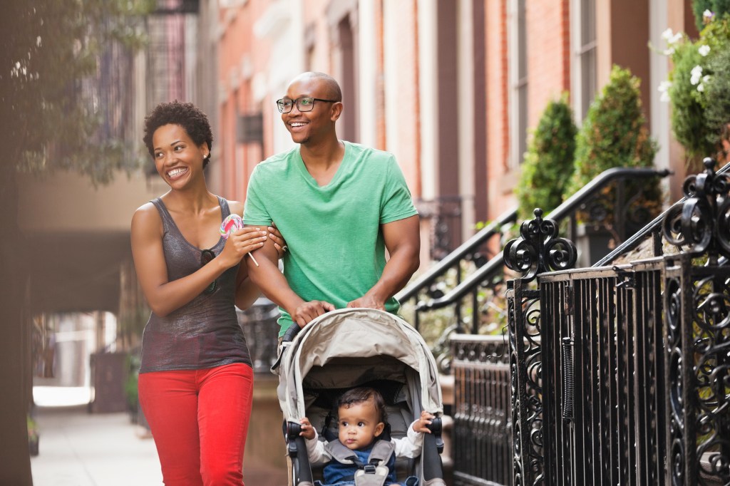 A happy family, mother, father and baby in a stroller, walking together on a city street.
