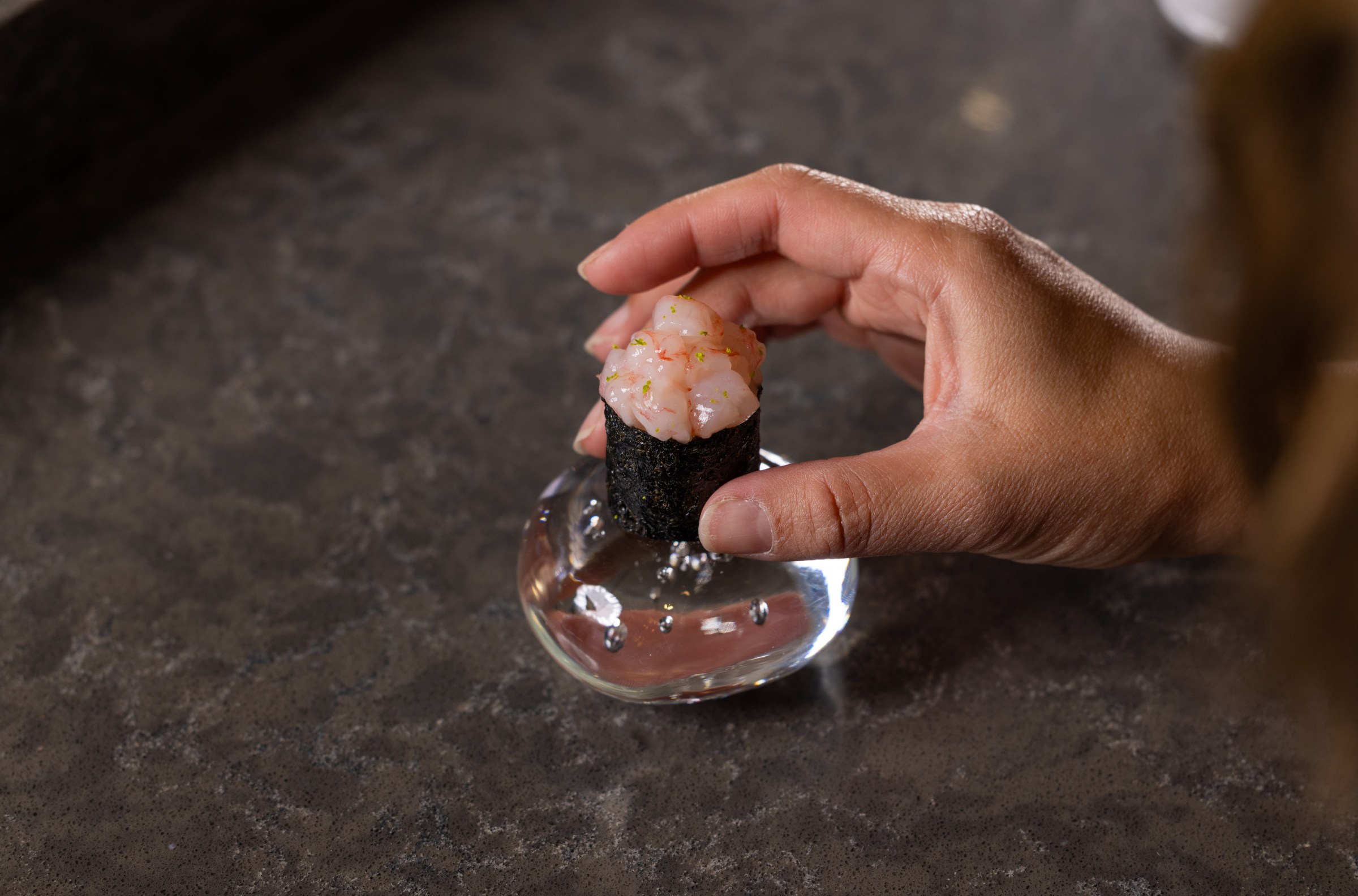 A hand assembles gimbap on a small dish.