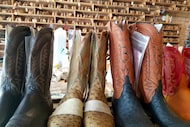 Boots in progress stand in front of a wall full of different sizes of boot foot forms at...