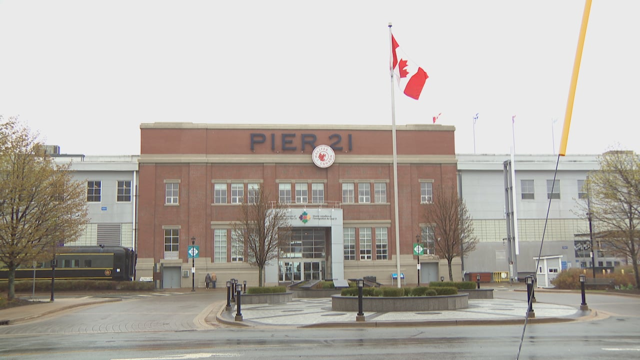 Pier 21 in Halifax is Canada's national museum of immigration. It is a brick building with a sign that says Pier 21 in block letters on the top centre of it. A Canadian flag flies in the front of it. 