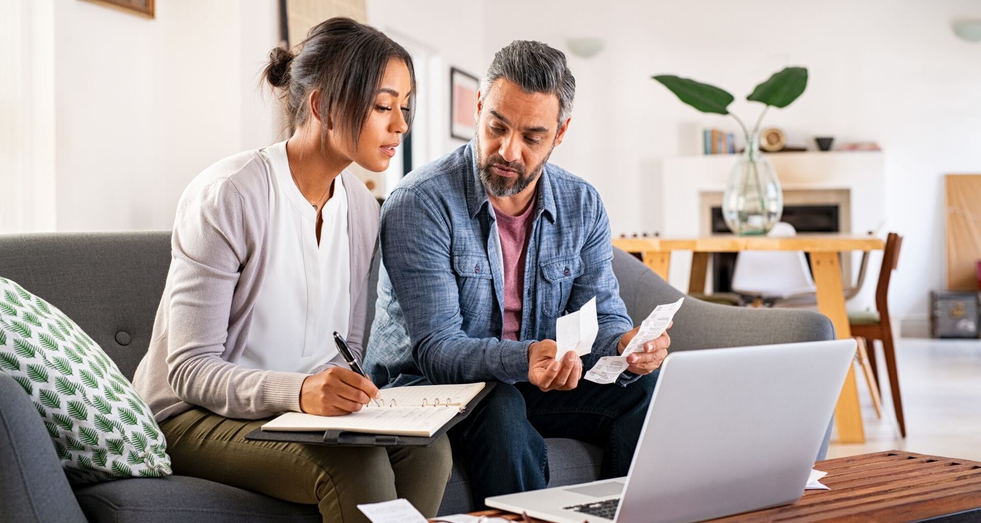 Mature couple calculating bills at home using laptop and calculator.