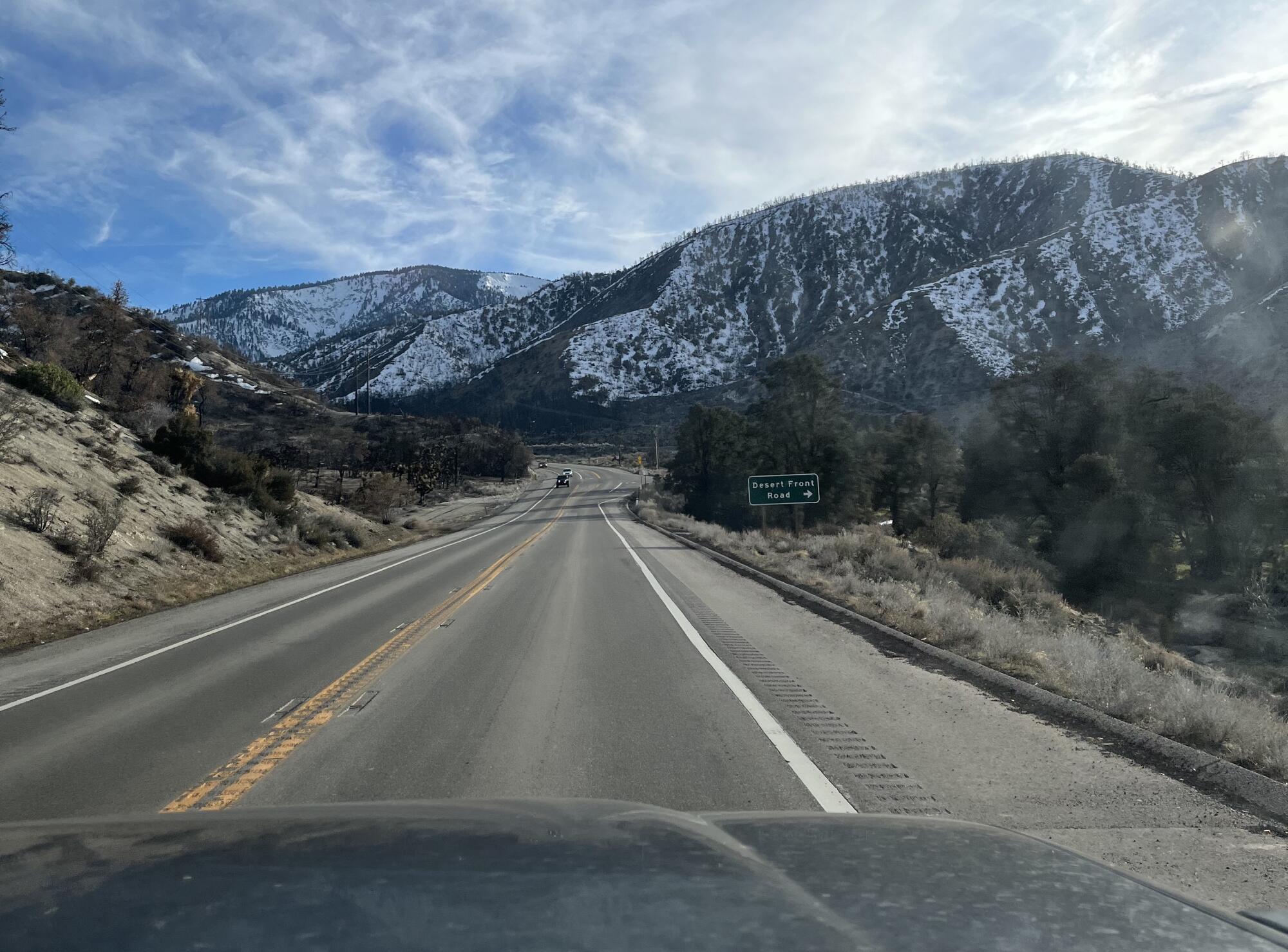 A view from a car driving up a road with snowy mountains in the distance.