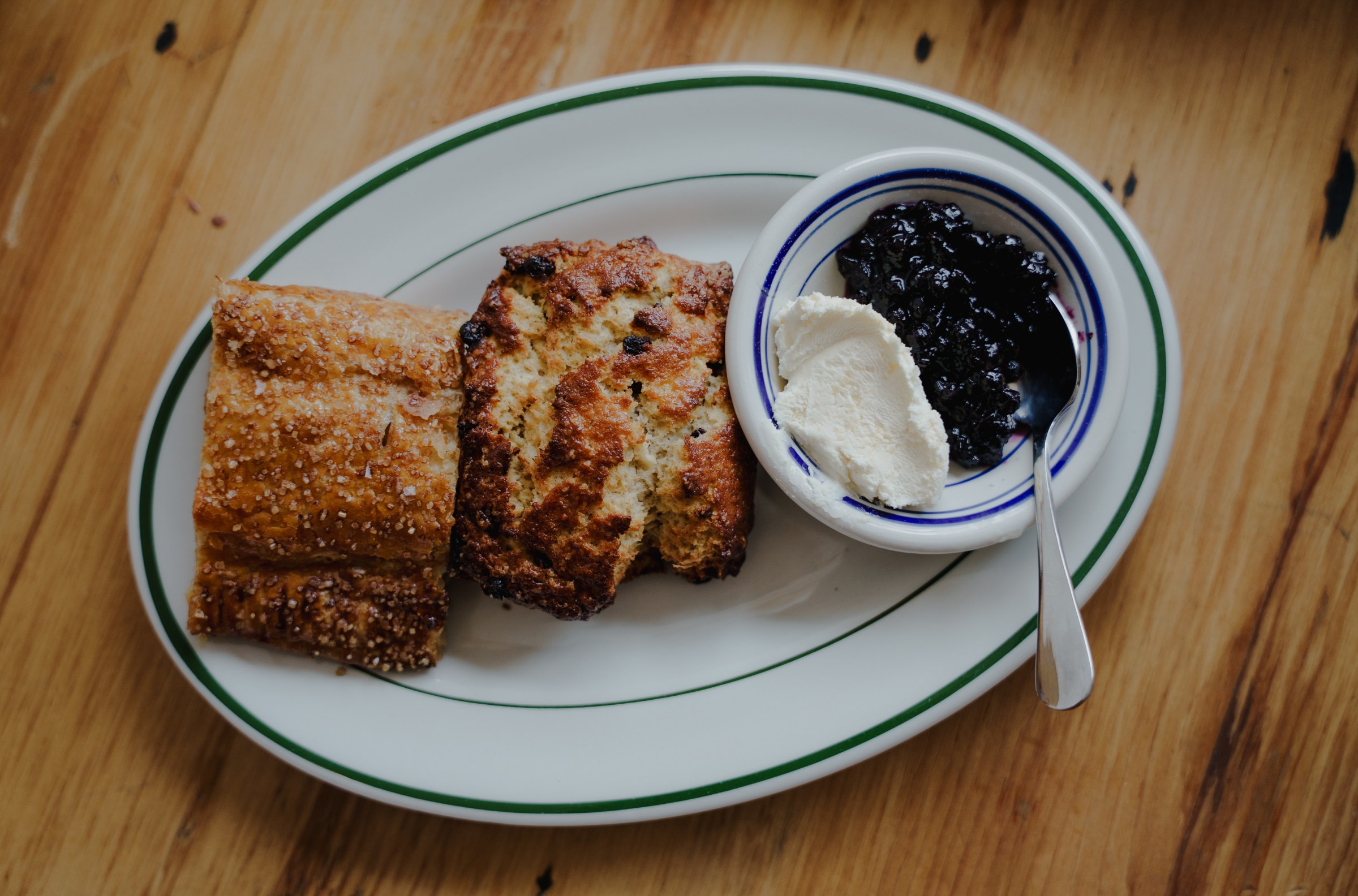 Two scones on a plate next to a condiment saucer of white cream and blueberry jam.