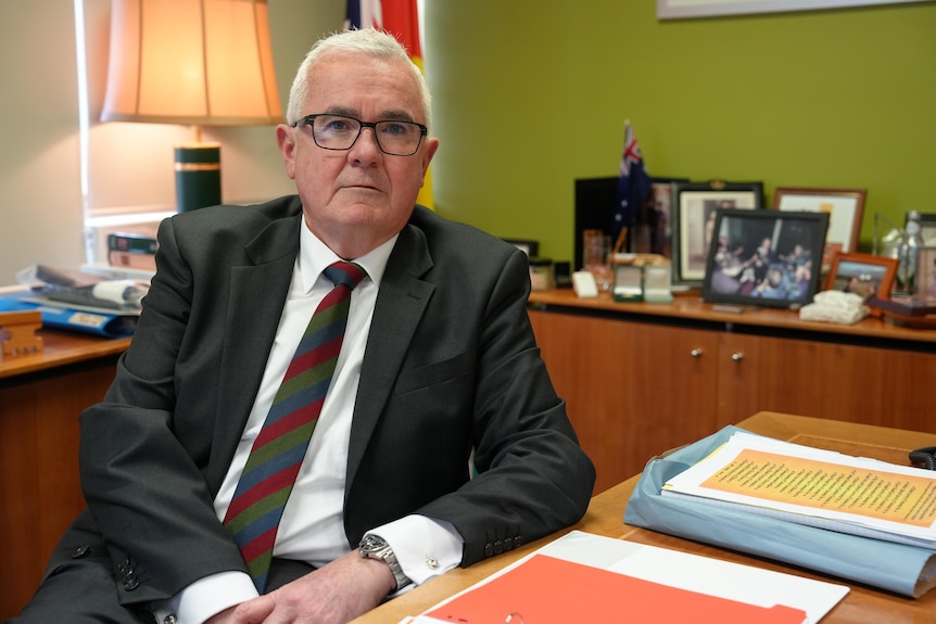 Andrew Wilkie sits at his desk, dressed in a suit and tie, looking into camera with a serious expression.