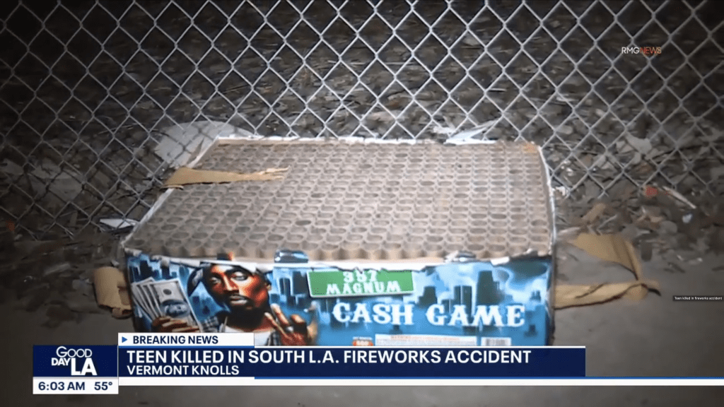 A partially exploded box of "Cash Game" fireworks behind a chain link fence.