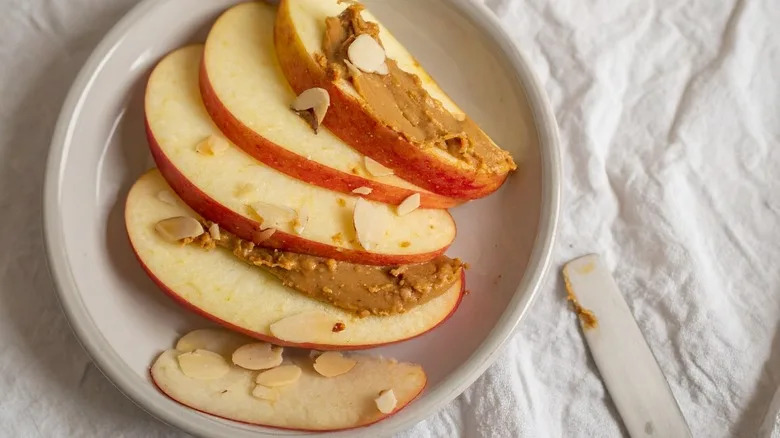 Apple slices topped with almond butter and slivered almonds on a white plate