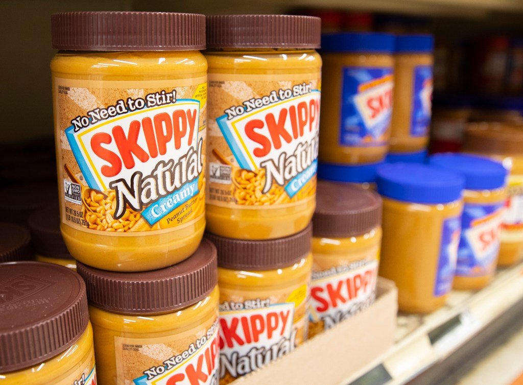 Containers of Skippy Natural Creamy peanut butter on a shelf.