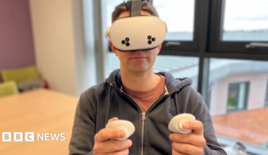 A man with short brown hair and glasses sits in a meeting room and smiles at the camera.