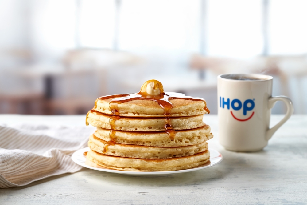 A stack of pancakes on a plate next to a cup of coffee.