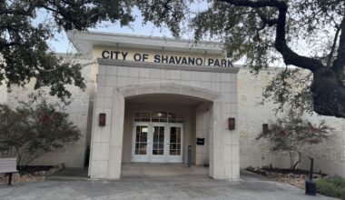 front exterior of a white city hall building surrounded by trees