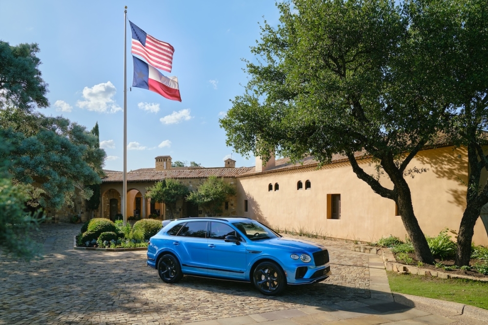 A blue Bentley car is seen parked outside of a home in Texas on a sunny day.