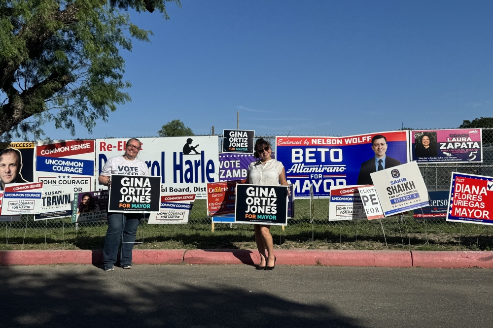 A group of people are seen holding up campaign signs during a runoff election on a sunny day in San Antonio, Texas.