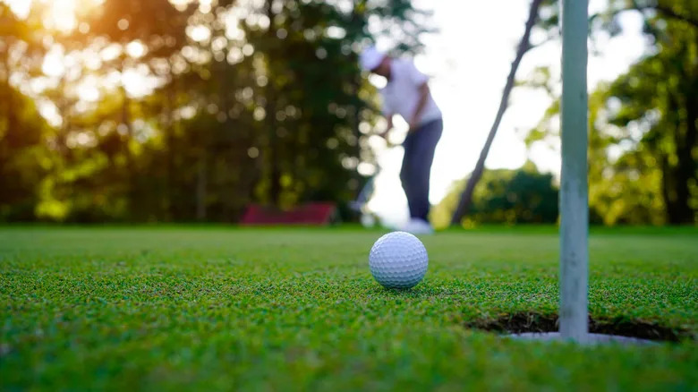 Close shot of a golf ball rolling to the hole with the golfer in the background