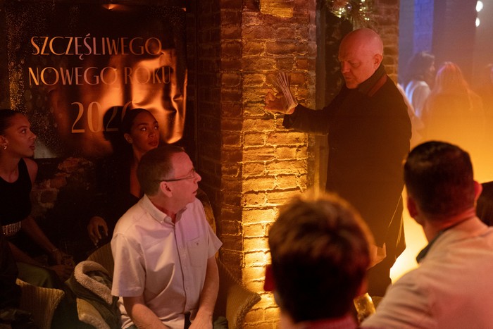 Max stands above Ian, Peter, Jack, Chelsea and Gina in a golden-lit Harry's Barn in EastEnders.