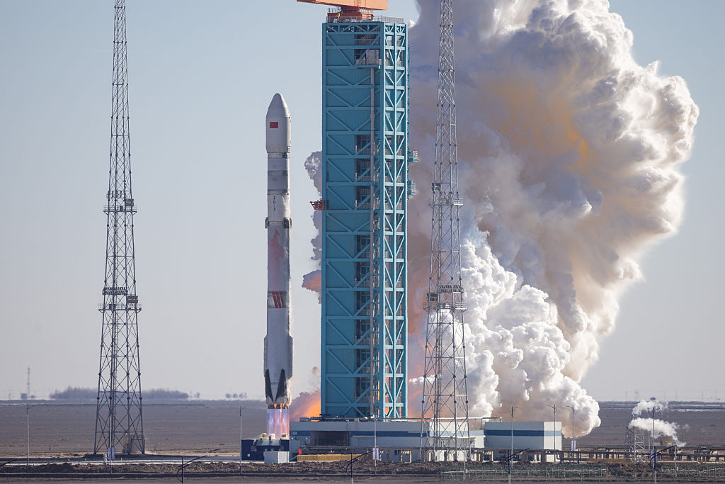 A tall white rocket launches from a pad with billowing white smoke in the background