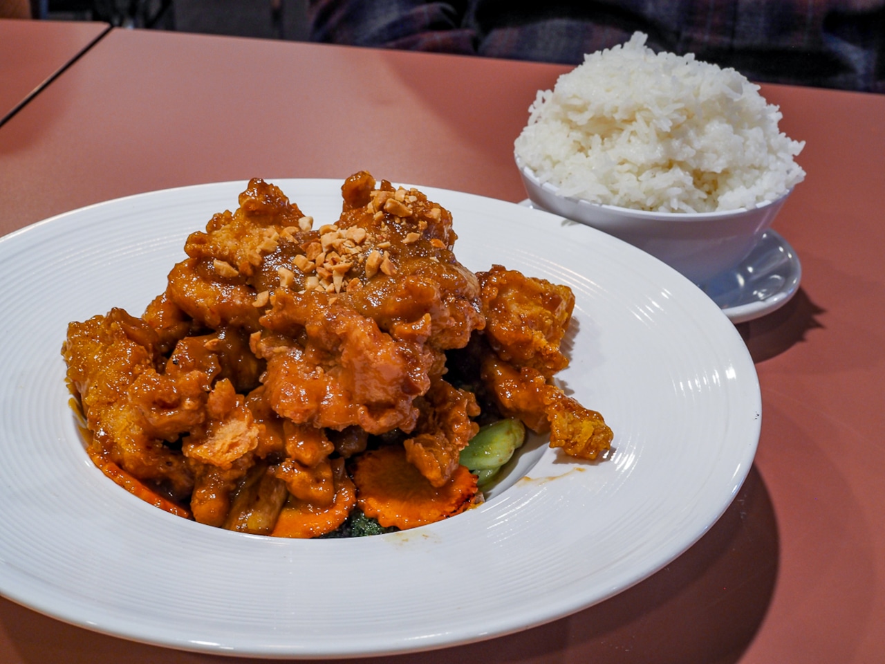 Wide rimmed, shallow white bowl filled with chicken and vegetables next to a bowl of rice