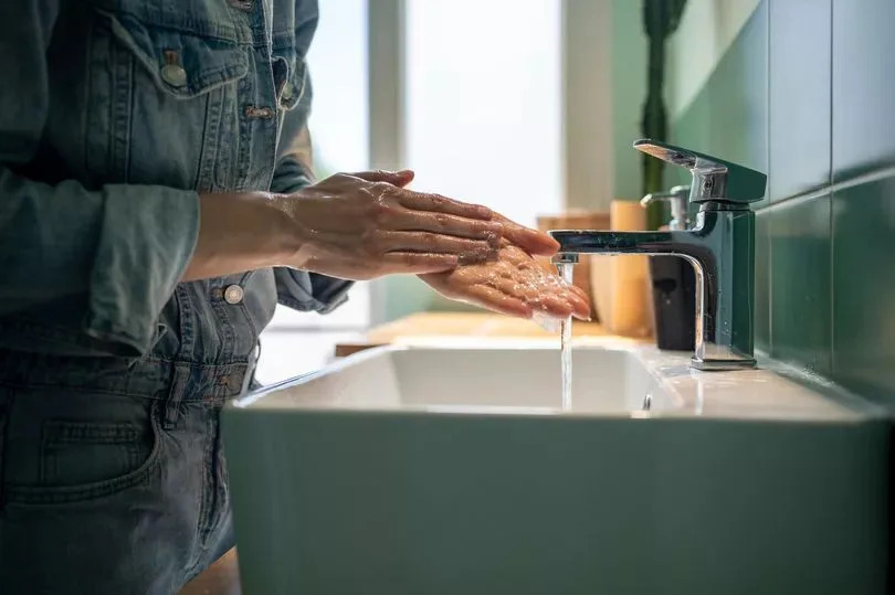 Unrecognizable woman washes hands with soap and foam in the sink on sunny day in bright bathrooms
