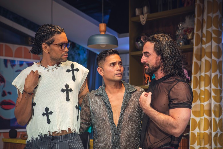 Three cast members look at each other  while wearing club attire. 