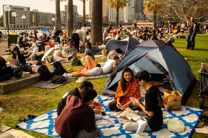 People in front of a tent and others sitting on a grass area in Sydney.