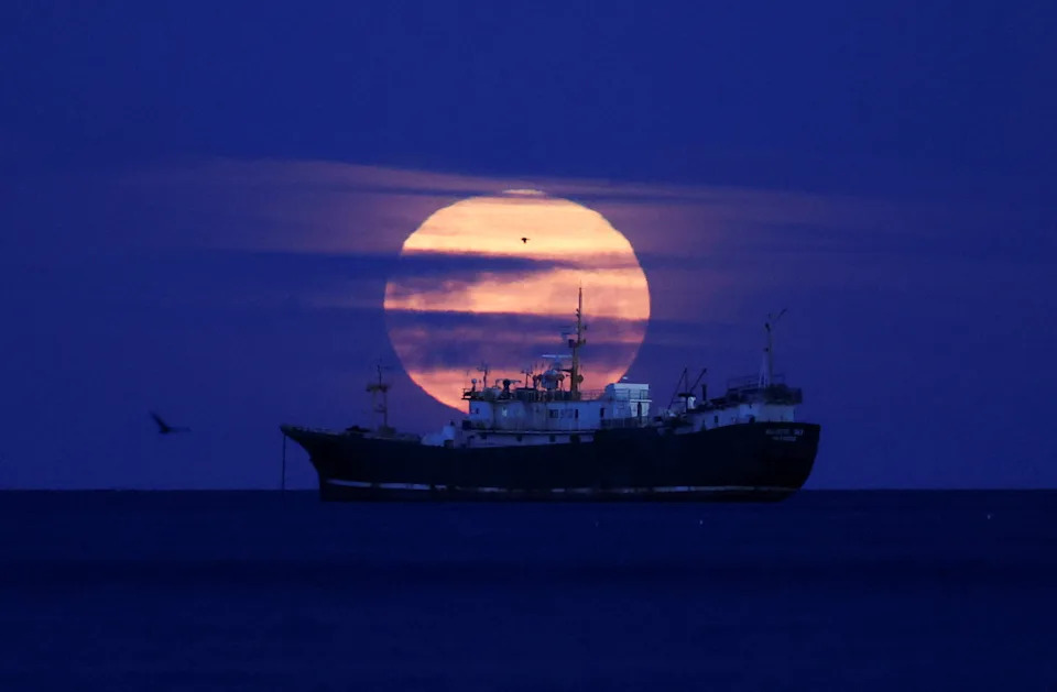 The cold moon, the last supermoon of 2025, illuminates the sky as a ship passes by, in the Strait of Magellan in Punta Arenas, Chile.