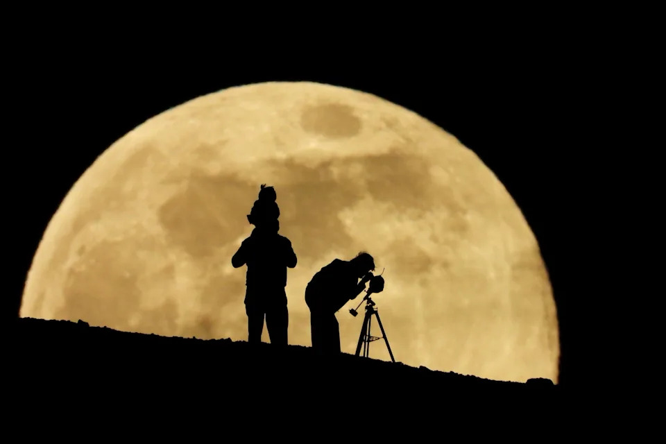 A couple and their daughter use a telescope to observe the last supermoon of 2025, in Aguimes, on the island of Gran Canaria, Spain.