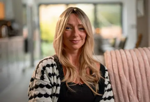 Ellen, a woman with long blonde hair, is sat on a sofa smiling at the camera