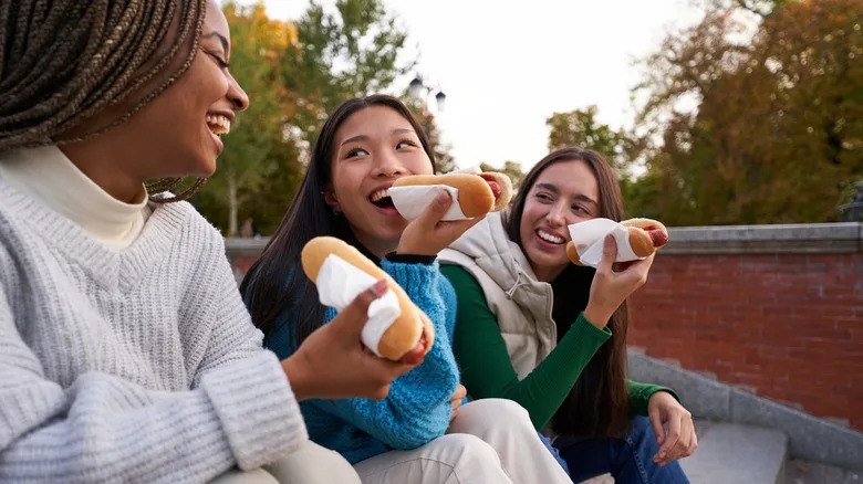 Group of three girls smiling while eating hot dogs