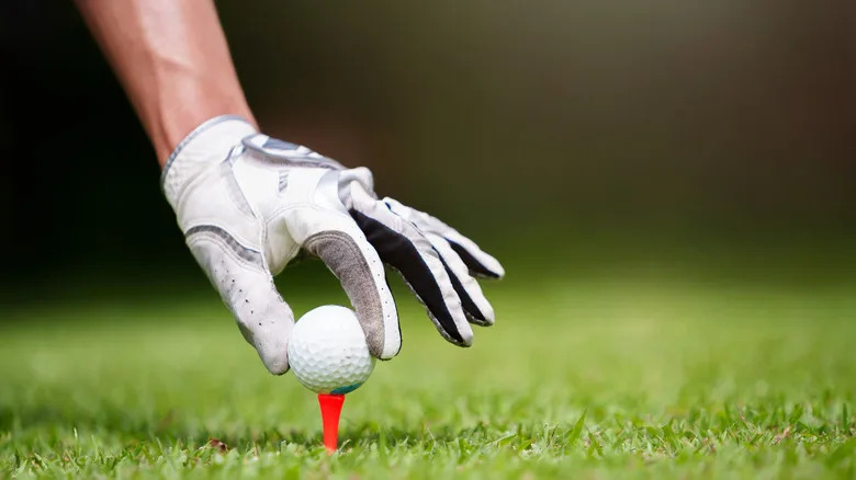 Golfer placing ball on tee with gloved hand